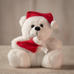 Small white stuffed teddy bear wearing a red Santa hat and holding a red stocking