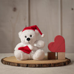 Small white stuffed teddy bear wearing a red Santa hat and holding a red stocking