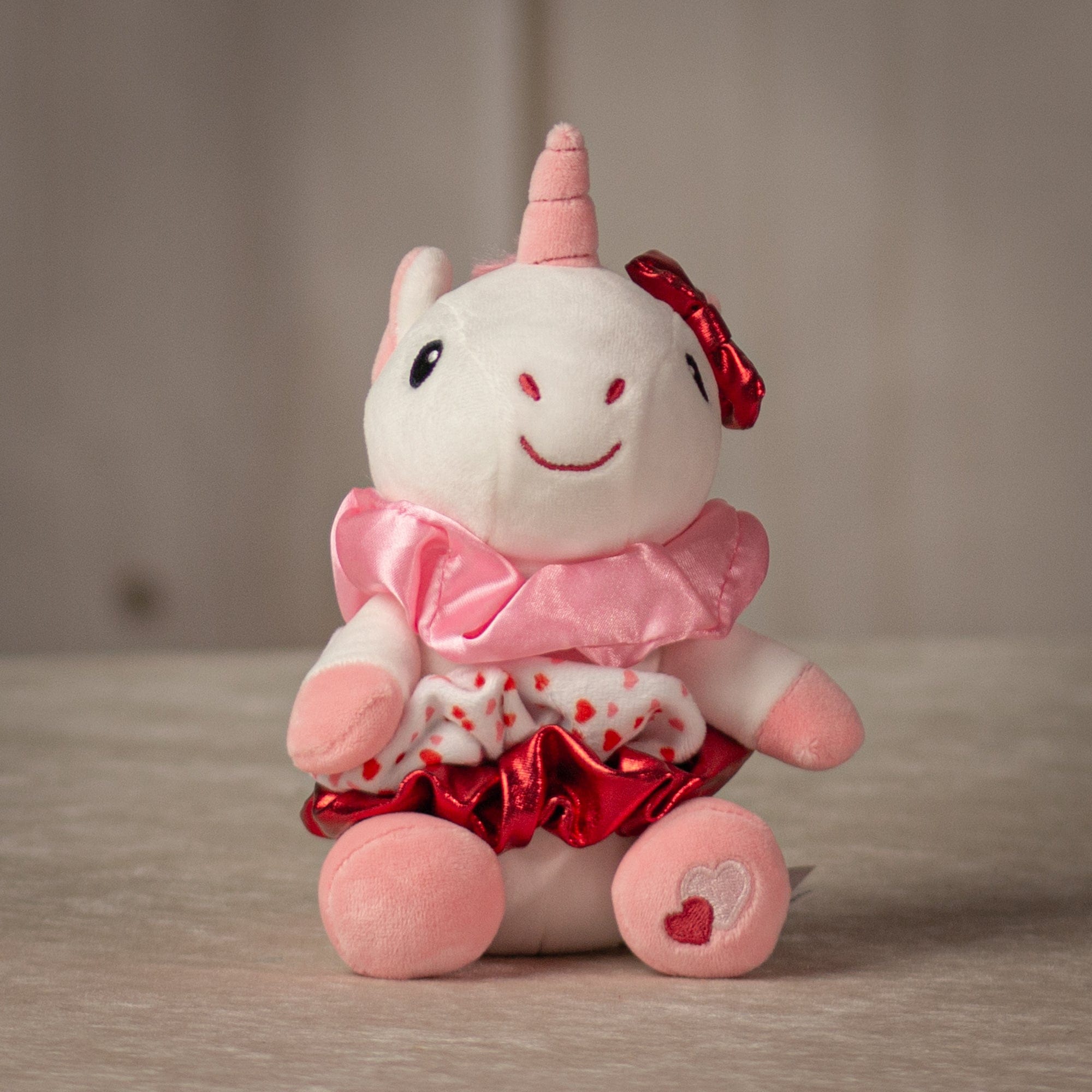 6" stuffed white unicorn keychain with three Valentine's designed hair scrunchies tied around its body
