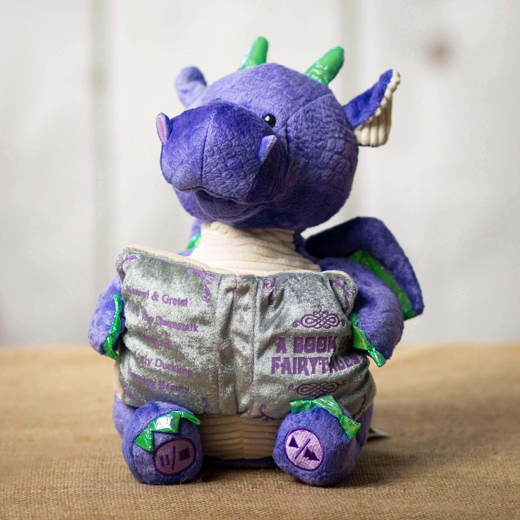 A purple animated dragon that is 10.5 inches tall while sitting holding a storytelling book