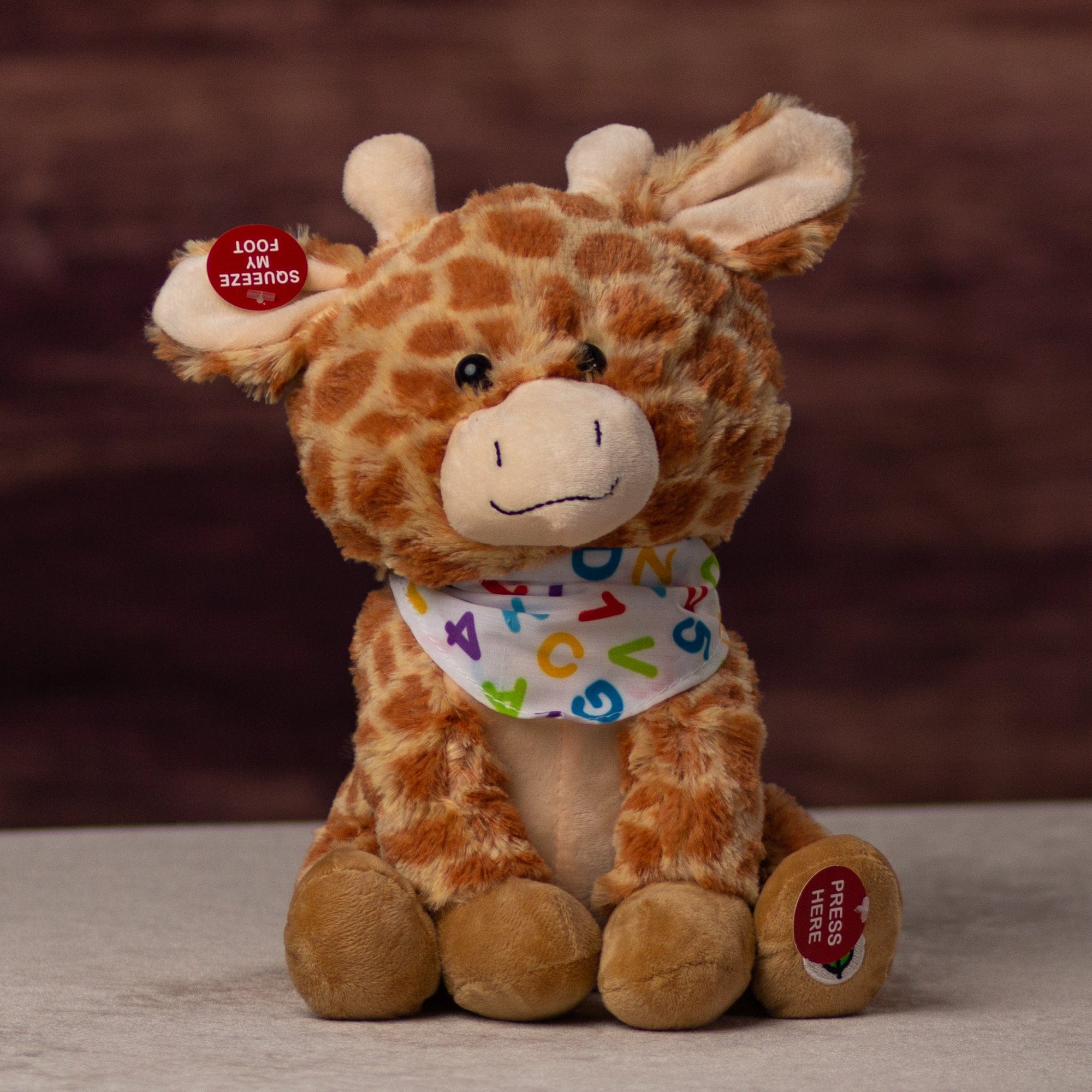 A spotted sitting giraffe that is 10 inches tall while sitting wearing a ABCs and 123s covered bandanna
