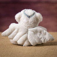 The back of white bear that is 6 inches tall while sitting wearing a pair of wings and a silver halo.