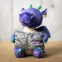 A purple animated dragon that is 10.5 inches tall while sitting holding a storytelling book