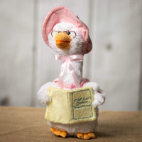 A white goose that is 14 inches tall while sitting wearing glasses and a light pink cap holding a nursery rhyme book