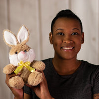 A woman holding a beige rabbit that is 7 inches while sitting wearing a yellow bow