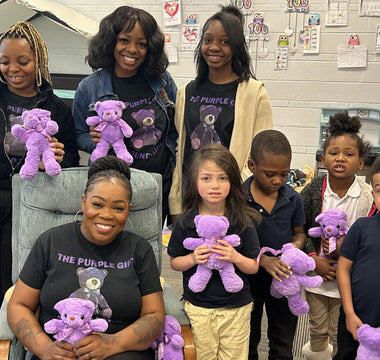 A group of smiling young children holding purple teddy bears in a classroom setting