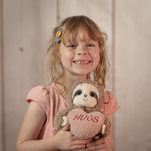 Little girl holding a 10" stuffed sloth that is holding a stuffed heart that says, "hugs".