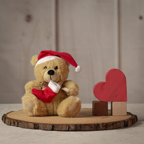 Small beige stuffed bear wearing a red Santa hat and holding a red stocking