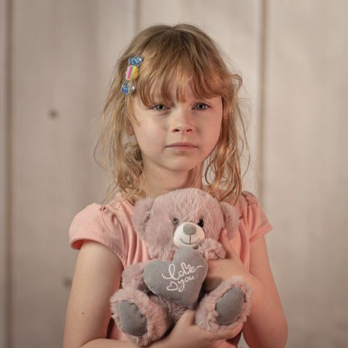 little girl holding a 7 inch dusty pink stuffed bear holding a stuffed heart that says, "I love you".