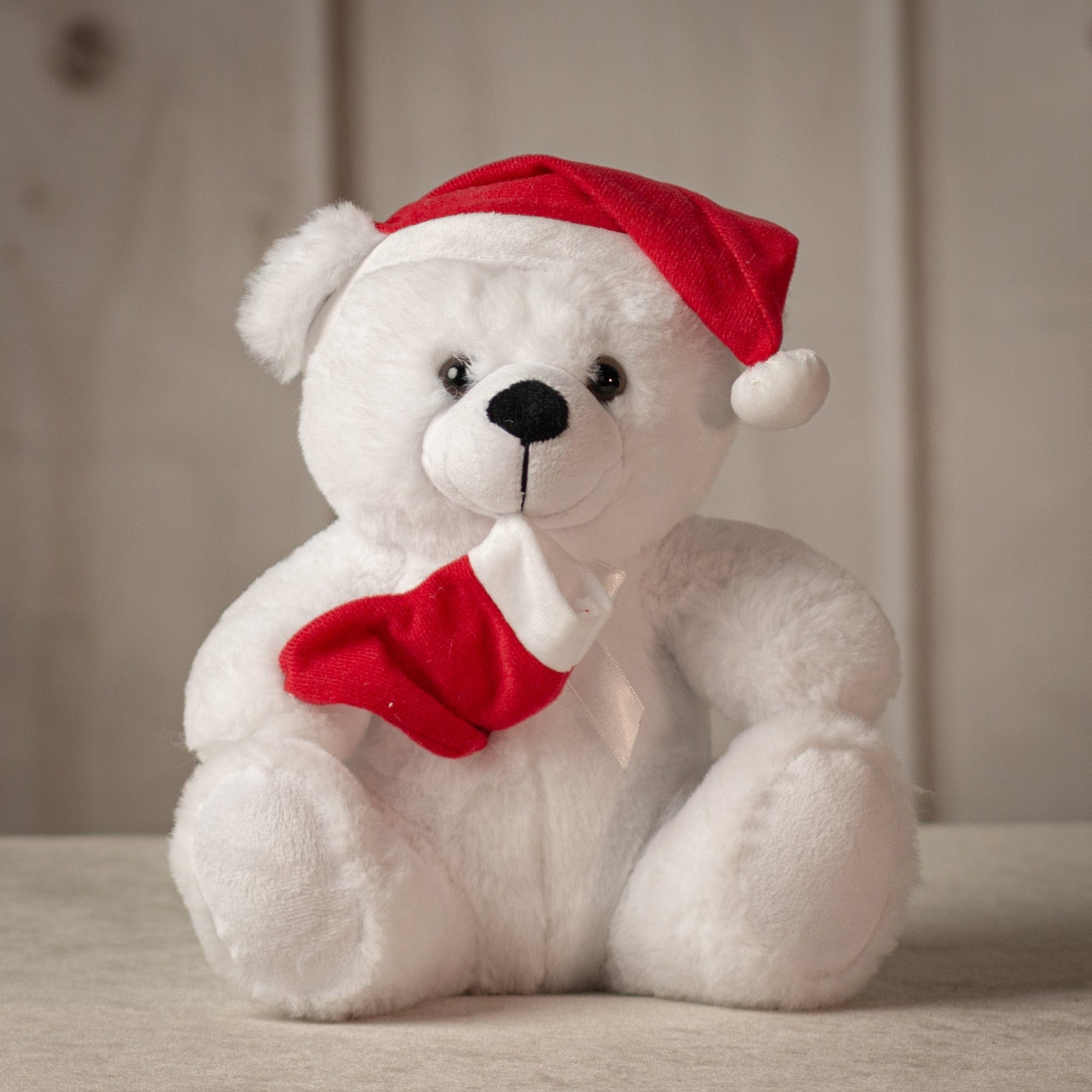 Medium sized white bear wearing a red Santa hat and holding a red stocking
