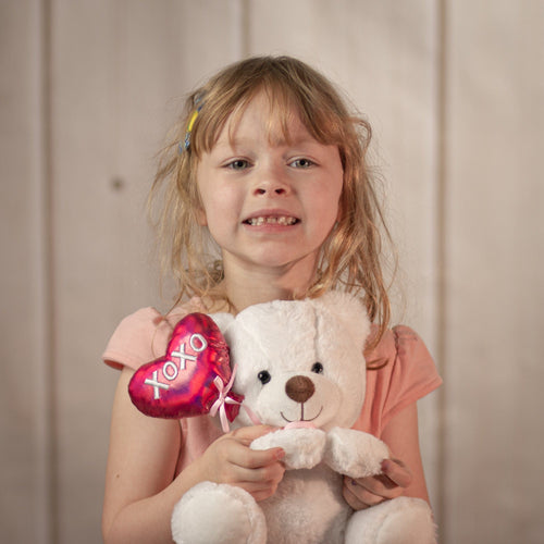 Little girl holding 9 inch white stuffed bear that is holding a heart balloon that says "xoxo"