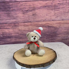 Small stuffed beige teddy bear with Christmas hat and red bow