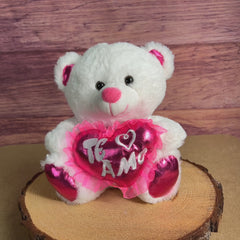 A white bear that is 10 inches tall while sitting with pink feet and ears holding a shiny pink "Te Amo" heart