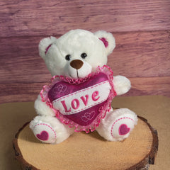 A white bear that is 10 inches tall while sitting with glittery feet and ears holding a glittery pink "LOVE" heart