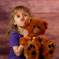 girl holding 12" stuffed brown bear wearing a bow