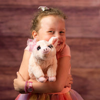 girl holding 12 in stuffed pink pig wearing a bow and has eyelashes