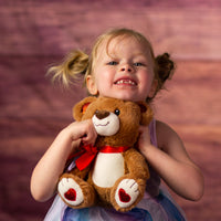 girl holding 9 in stuffed brown valentines bear with glitter ears and heart paws and wearing a bow