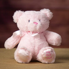 A sitting pink bear that is 10 inches tall while standing with "My First Bear" on its left paw