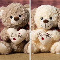 A brown bear and a cream colored dog with brown ears that are 10 inches tall while sitting holding a cream heart