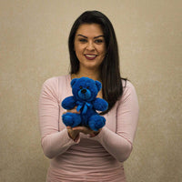 A woman holds a blue bear that is 6 inches tall while sitting