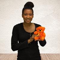 A woman holds a orange bear that is 6 inches tall while sitting