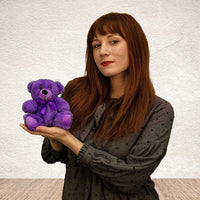 A woman holds a purple bear that is 6 inches tall while sitting