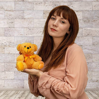 A woman holds a orange bear that is 6 inches tall while sitting