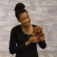A  woman holds a brown bear that is 6 inches tall while sitting