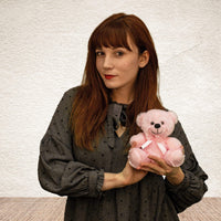 A woman holds a pink bear that is 6 inches tall while sitting