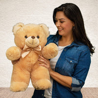A woman holds a beige bear that is 18 inches tall while standing