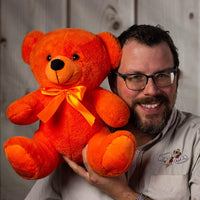 A man holds a bright orange bear that's 14 inches tall while sitting