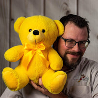 A man holds a yellow bear that's 14 inches tall while sitting