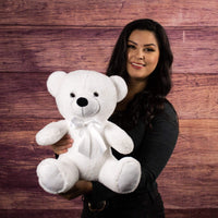 A woman holds a white bear that is 14 inches tall while sitting wearing a matching bow