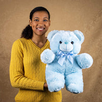 A woman holds a blue bear that is 18 inches tall while standing