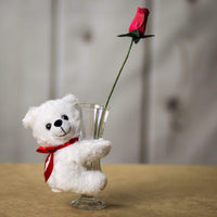 A white bear that is 5.5 inches tall while sitting hugging a vase