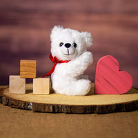 A white bear that is 5.5 inches tall while sitting on top of a piece of wood