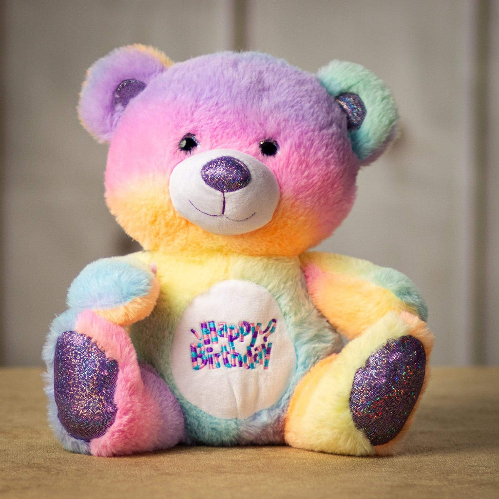 A rainbow colored bear that is 10.5 inches tall while sitting with "Happy Birthday" embroidered on the chest