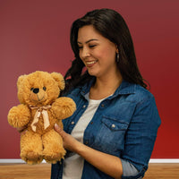A woman holds a beige bear that is 12 inches tall while standing