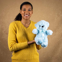A woman holds a blue bear that is 12 inches tall while standing