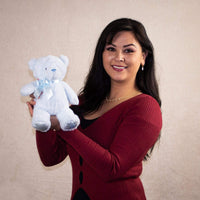 A woman holds a blue bear that is 10 inches tall while standing with "My First Bear" on its left paw