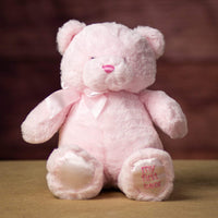 A sitting pink bear that is 15 inches tall while standing with "My First Bear" on its left paw