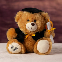 A brown bear sporting a cape, diploma, hat and even the words #1 Grad embroidered on a paw