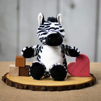 A black and white stripped zebra that is 13 inches tall while standing on top of a piece of wood