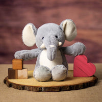 A gray elephant that is 13 inches tall while standing in a sitting position on top of a piece of wood
