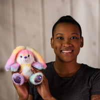 A woman holding a rainbow bunny that is 6 inches tall while sitting with shiny feet and nose