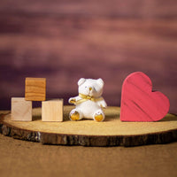 A white bear that is 3.5 inches tall while sitting with a gold bow and paws on top of a piece of wood