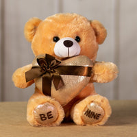 A beige bear that is 11 inches tall while sitting holding a shiny gold gift-wrapped heart with BE MINE embroidered on its feet
