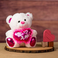 A white bear that is 10 inches tall while sitting with pink feet and ears holding a shiny pink "Te Amo" heart next to wooden blocks