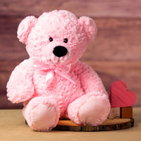 A pink bear that is 22 inches tall while standing wearing a matching bow next to wooden blocks