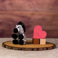 A black and white stripped zebra that is 5 inches tall while sitting next to wooden blocks